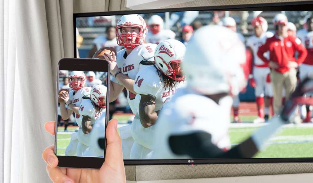 A hand holding an iPhone that is mirroring an image of american football to an LG TV