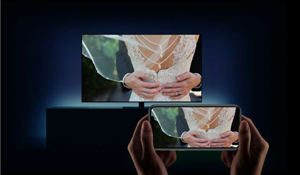 person mirroring an image of bride and groom embracing from an iPhone to Smart TV in a darkened room